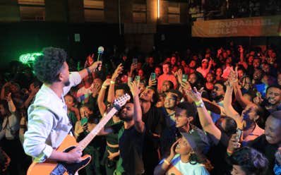 Zeruabbel Molla at live concert performing on stage with a guitar, engaging a lively crowd.