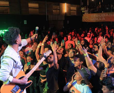 Zeruabbel Molla performing on stage with a guitar, engaging a lively crowd.