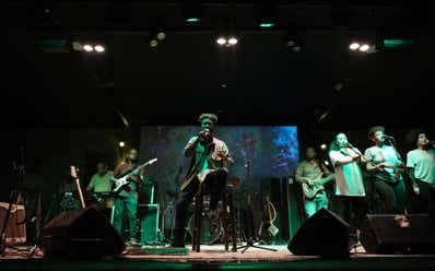 Zeruabbel Molla's band performing on stage with a singer at the center, surrounded by musicians playing guitars and other instruments, under stage lighting.