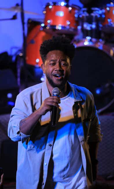 Zeruabbel Molla singing on stage with a microphone, drums in the background.