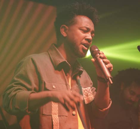 Zeruabbel Molla singing into a microphone on stage with colorful lighting.